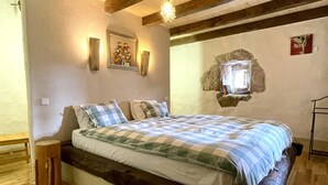 Ein Schlafzimmer mit einem hölzernen Bett, Holzboden, einer Wanddekoration aus Stein und einem kleinen Tisch.