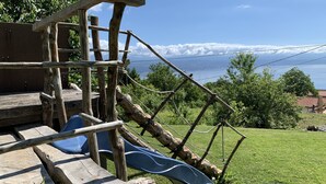Ein Spielplatz aus Holz mit Rutsche und Klettergerüsten, vor einer Kulisse aus blauem Himmel und fernen Bergen.