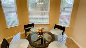 Une table de salle à manger ronde en verre, accompagnée de quatre chaises, d’un chandelier central et d’un lustre.