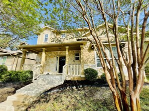 A two-story house with a stone facade, a front porch with columns, and a small front yard with a tree and shrubs. - 3BR ~ MID & STR Corporate rental Pet friendly home ~ Kalahari-Dell ~ mins to ATX (Round Rock)