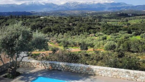 Una piscina con un muro de piedra, rodeada de olivos y vistas a montañas lejanas.