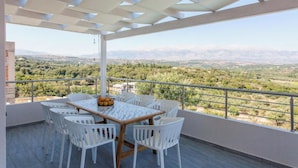 Un balcón con mesa y sillas, vista a un paisaje montañoso y una pérgola.
