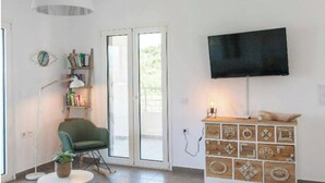 Una sala de estar con un sillón verde, una estantería, un televisor sobre un mueble de madera y un ventanal corredero.