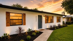 Une maison moderne à l’extérieur blanc, portant le numéro 2532, avec de grandes fenêtres dotées de volets en bois, un chemin en béton et une pelouse bien entretenue.