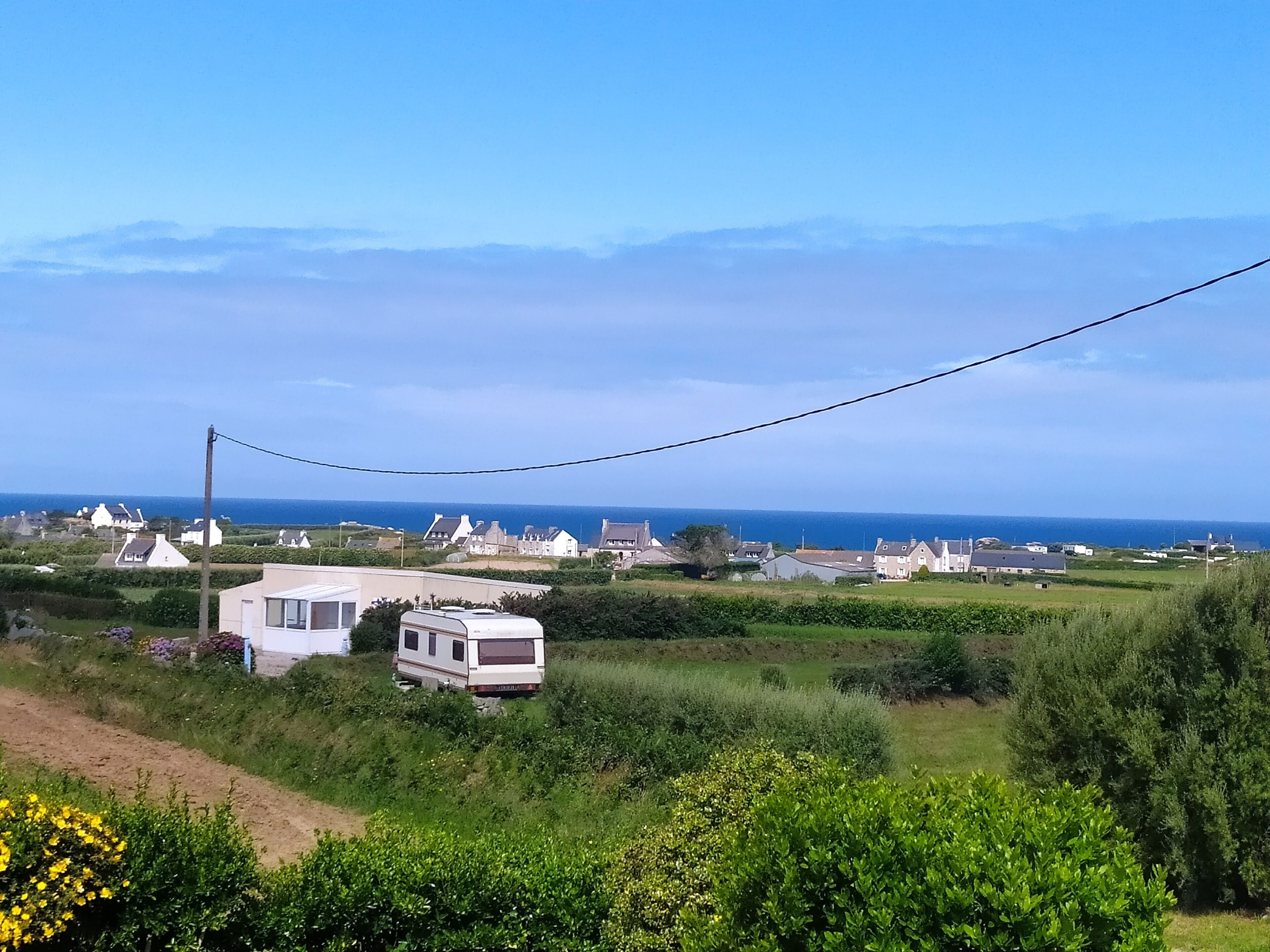 Een camping met meerdere caravans en huisjes, omgeven door groen en een helder uitzicht op zee.