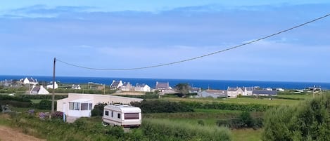 Een camping met meerdere caravans en huisjes, omgeven door groen en een helder uitzicht op zee.