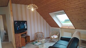 A cozy living room with a television, wicker chairs, a glass coffee table, and a sloped ceiling with a skylight. - Furnished, 2 stars, with sea view (Plouescat)