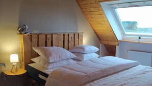 A cozy bedroom with a sloped ceiling, a wooden headboard, a large bed with white bedding, a bedside lamp, and a skylight. - Furnished, 2 stars, with sea view (Plouescat)