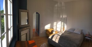 Ein Schlafzimmer mit einem Bett, einem Sessel, einem Nachttisch, einem Spiegel und einem Kamin.