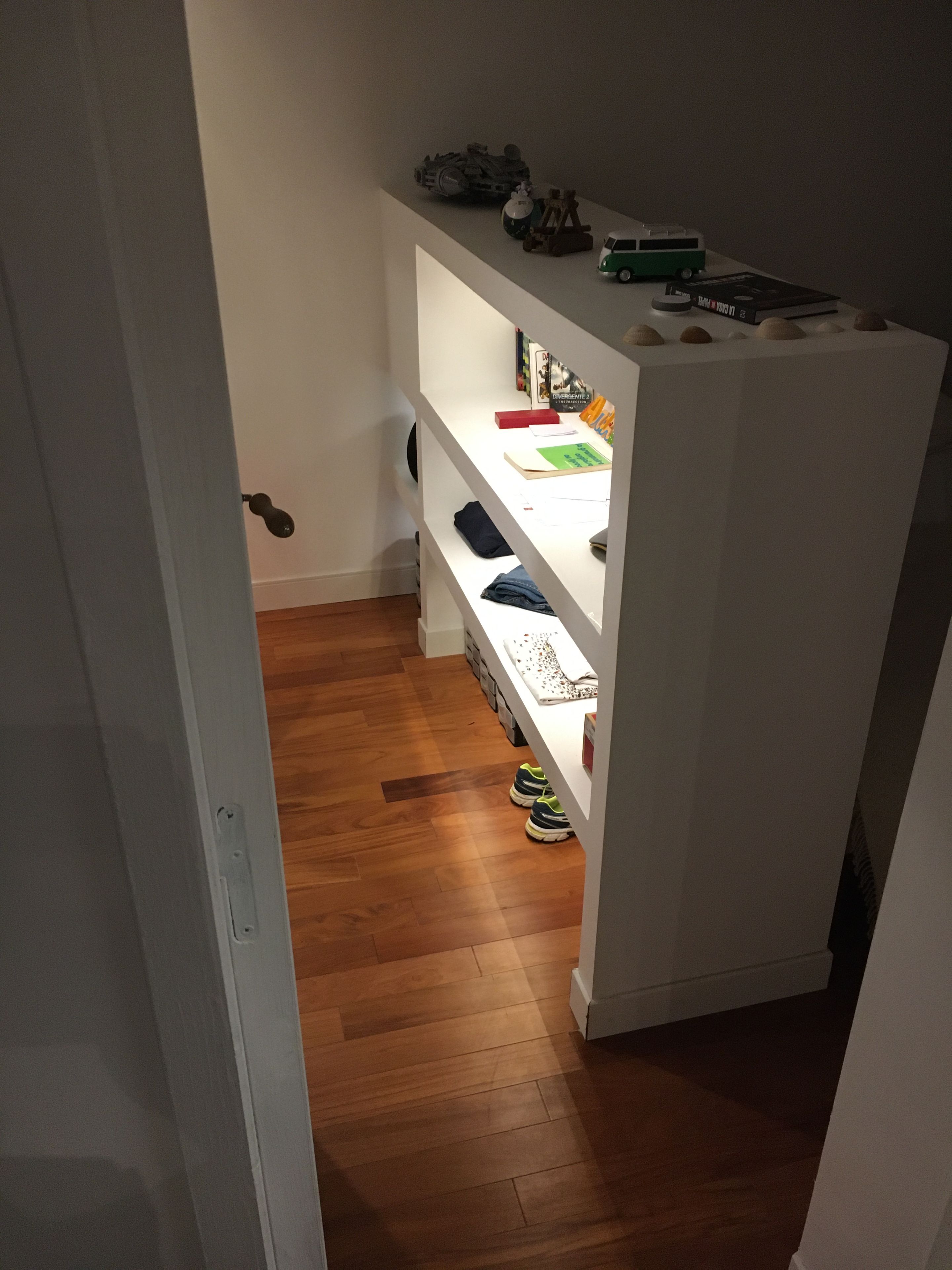 Een smalle gang met een houten vloer die leidt naar een witte berging met planken.