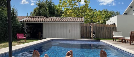 A swimming pool with a tiled edge, a wooden deck, and a red bench.