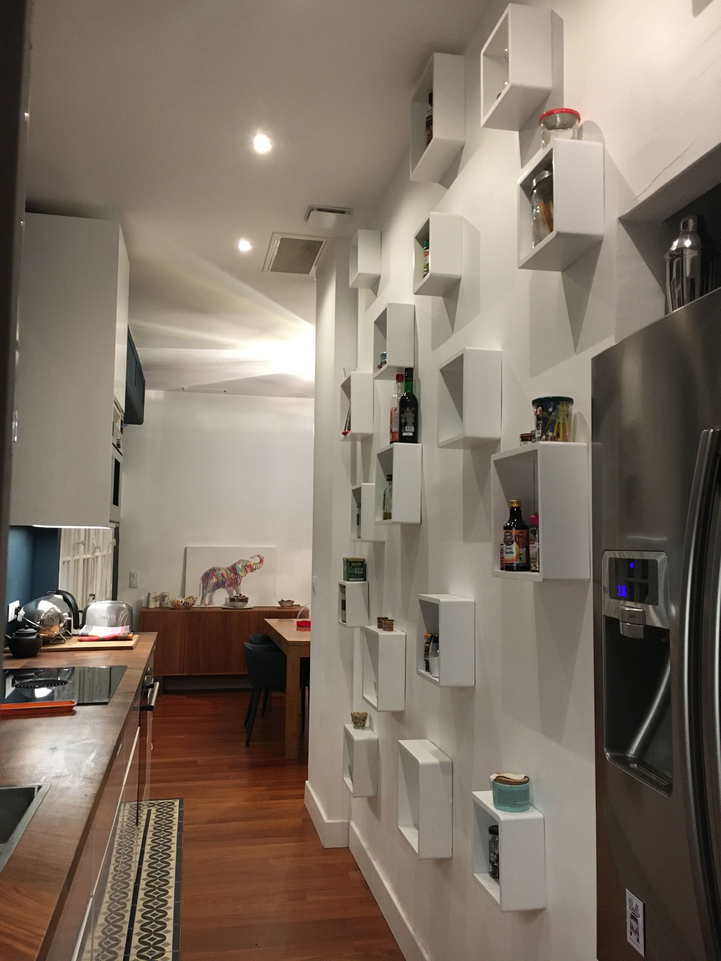 A modern kitchen with built-in shelves, a stainless steel refrigerator, and a wooden dining table.