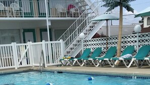 A swimming pool with a lifeguard chair, lounge chairs, and a staircase leading to a balcony. - The Townhouse Cozy Ocean-front first floor condominium. (Wildwood Crest)
