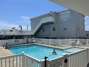 A swimming pool with a white fence, a lifeguard stand, and a building with a balcony.