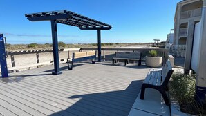 A wooden deck with benches and a pergola, overlooking a beach. - The Townhouse Cozy Ocean-front first floor condominium. (Wildwood Crest)