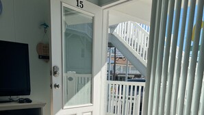 A room with a door labeled '15', a white-framed window, a white door with a keypad, a television on a cabinet, and a patterned doormat. - The Townhouse Cozy Ocean-front first floor condominium. (Wildwood Crest)