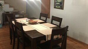Un comedor con una mesa y sillas de madera, una lámpara colgante, un cuadro en la pared y una escalera al fondo.