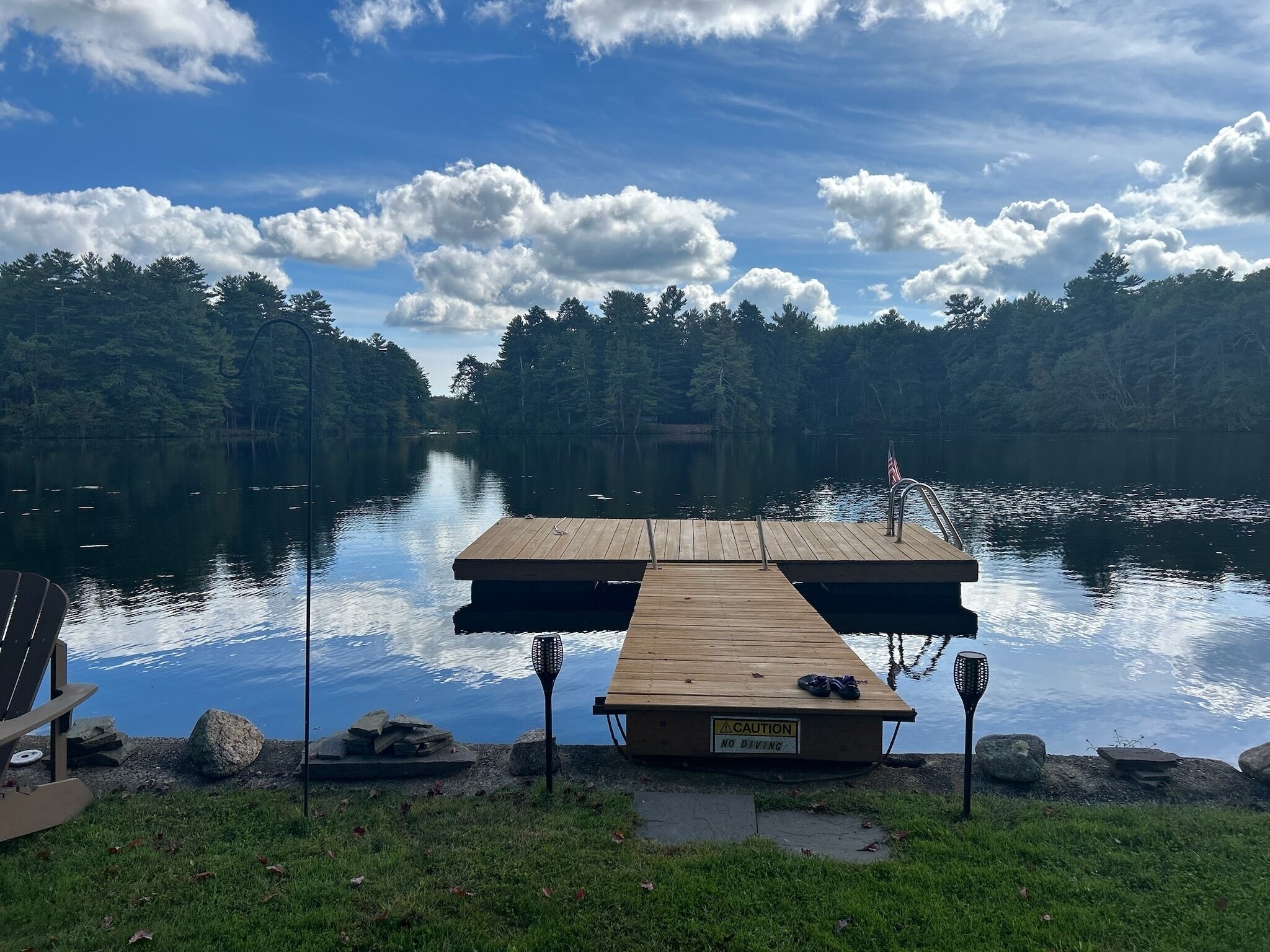 Une jetée en bois s’avance sur un lac paisible, entouré d’une forêt dense. Un panneau d’avertissement sur la jetée indique : « IL EST INTERDIT DE PLONGER ».