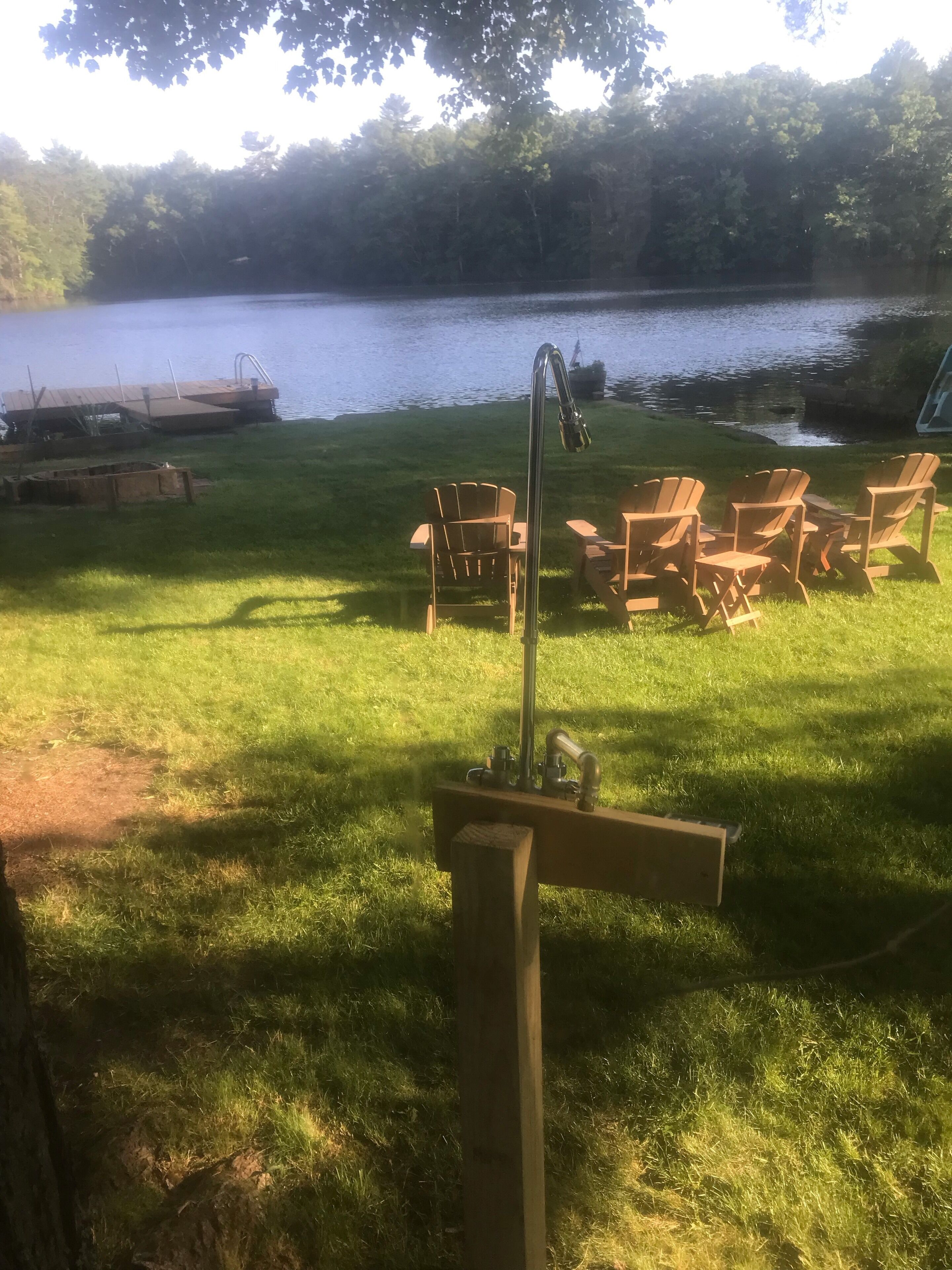 Un espace extérieur aménagé au bord du lac, avec des chaises en bois et un foyer métallique.