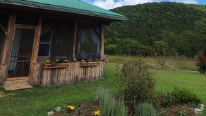 A rustic wooden cabin with a green roof, surrounded by a well-maintained garden and a clear blue sky with scattered clouds. - Riverside "Barndominium" w/ easy access to water (Eureka Springs)
