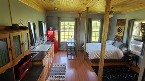 A compact room with a bed, a small table, a red refrigerator, a sink, and a window with curtains. - Riverside "Barndominium" w/ easy access to water (Eureka Springs)
