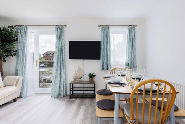 A dining area with a table set for four, a television mounted on the wall, and a view through the glass door.