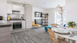 A modern kitchen with built-in appliances, a dining area with wicker chairs, and a large window providing natural light. - Seas the Day - Moments from Hamworthy Beach (Poole)