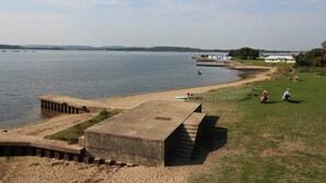 A waterfront area with a concrete pier, grassy banks, and a distant view of boats on the water. - Ocean Breeze - Two Bedroom Apartment with Parking (Poole)