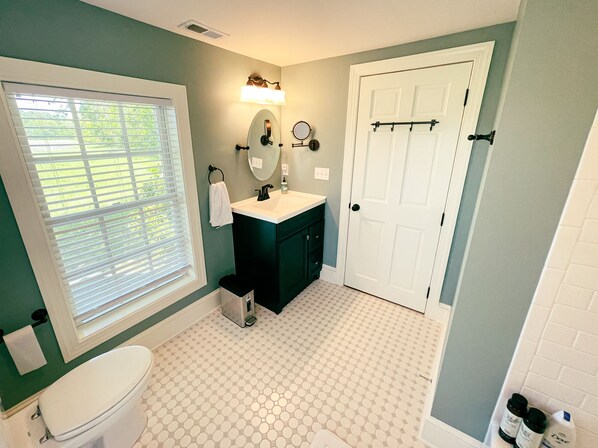 A bathroom with a toilet, sink, mirror, and a white door. - Cape Charles VA retreat with game arcade 👾, fire pit 🔥, Peloton 🚴🏽‍♀️, EV🔋 (Cape Charles)