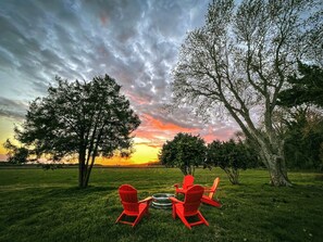 Vista del atardecer con dos sillas Adirondack rojas y una parrilla metálica en un campo de césped.