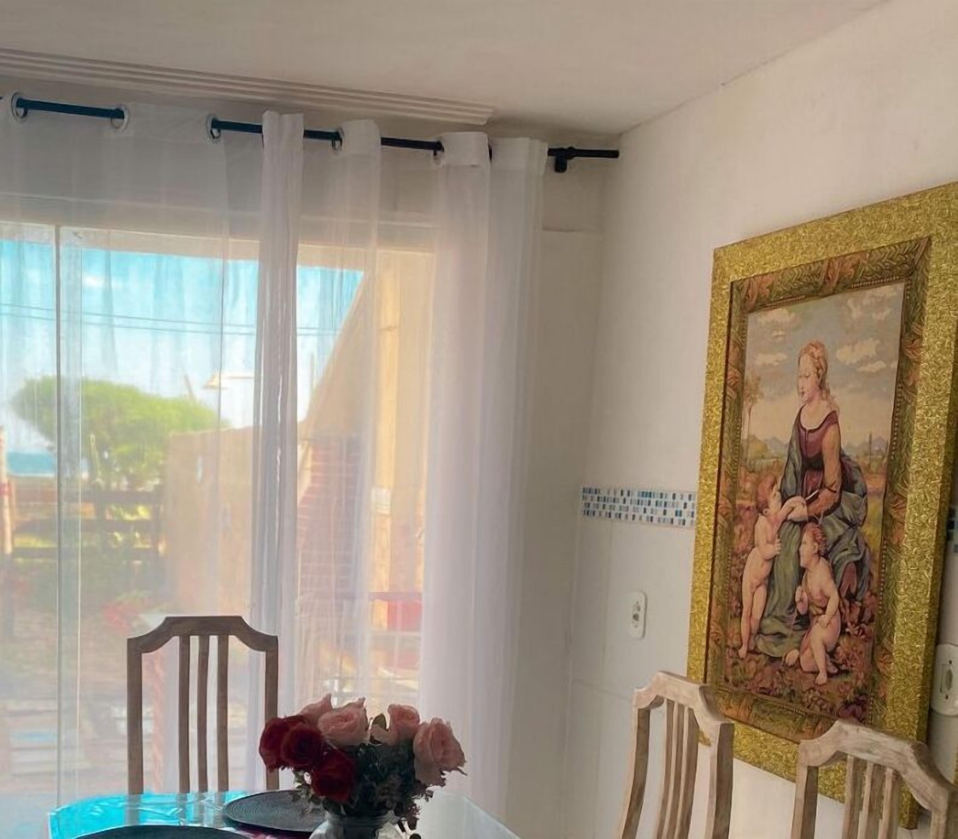 A dining area with a table, chairs, a vase of flowers, and a painting on the wall.