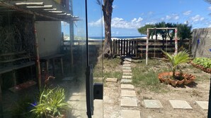 A courtyard with a stone pathway leading to a wooden gate, surrounded by potted plants and a view of the ocean. - Feet in the Sand. (Arraial do Cabo)