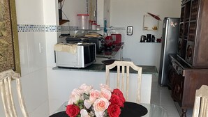 A dining area with a red tablecloth, black placemats, and a vase of flowers. There are chairs around the table, and a kitchen is visible in the background. - Feet in the Sand. (Arraial do Cabo)