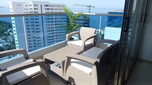Un balcón con mobiliario de mimbre y vistas a la ciudad y al océano.