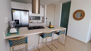 Una cocina moderna con gabinetes blancos, una campana extractora de acero inoxidable, una estufa empotrada y una pequeña isla con taburetes de bar.
