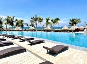 A poolside area with lounge chairs, palm trees, and a clear view of the ocean. - SANTA MARTA BEST OCEAN FRONT RESORT  FOR THE WHOLE FAMILY IN POZOS COLORADOS . (Santa Marta)