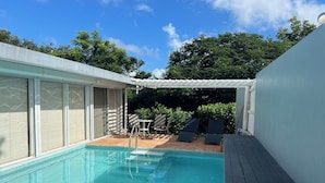 A swimming pool with a pergola, lounge chairs, and a table in a backyard setting.