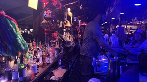 A bar area with a bartender preparing drinks, shelves stocked with bottles, and a counter with various items.