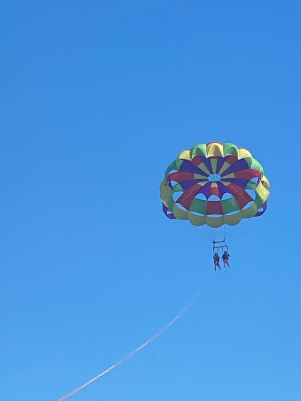 A colorful parasail with two people attached, flying against a clear blue sky. - Romantic Private Pool Villa @ Sapphire. Generator.Grill (Red Hook)