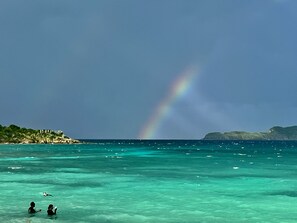 A beach with clear turquoise water, a rainbow, and a distant island with buildings. - Romantic Private Pool Villa @ Sapphire. Generator.Grill (Red Hook)