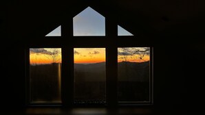 A room with three windows, each offering a view of a sunset over a mountainous landscape. -  Long Range Mtn View Hottub Game Room Firepit Grill Fireplace close to Asheville (Fairview)