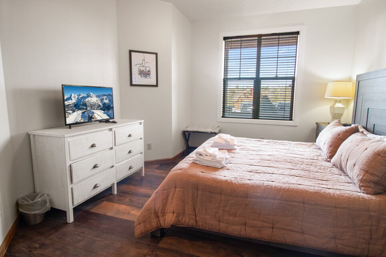 A bedroom with a bed, a dresser, a window with blinds, and a painting on the wall.