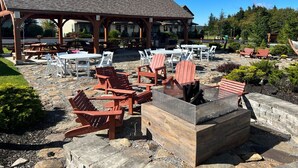 Ein Außenbereich mit Holz-Adirondack-Stühlen und Picknicktischen, einem überdachten Pavillon und einer Steinkaminfeuerstelle.