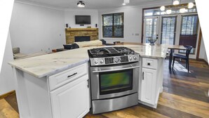 Eine Küche mit einer zentralen Kochinsel, weißen Schränken, einem eingebauten Backofen und einem Kamin aus Stein.