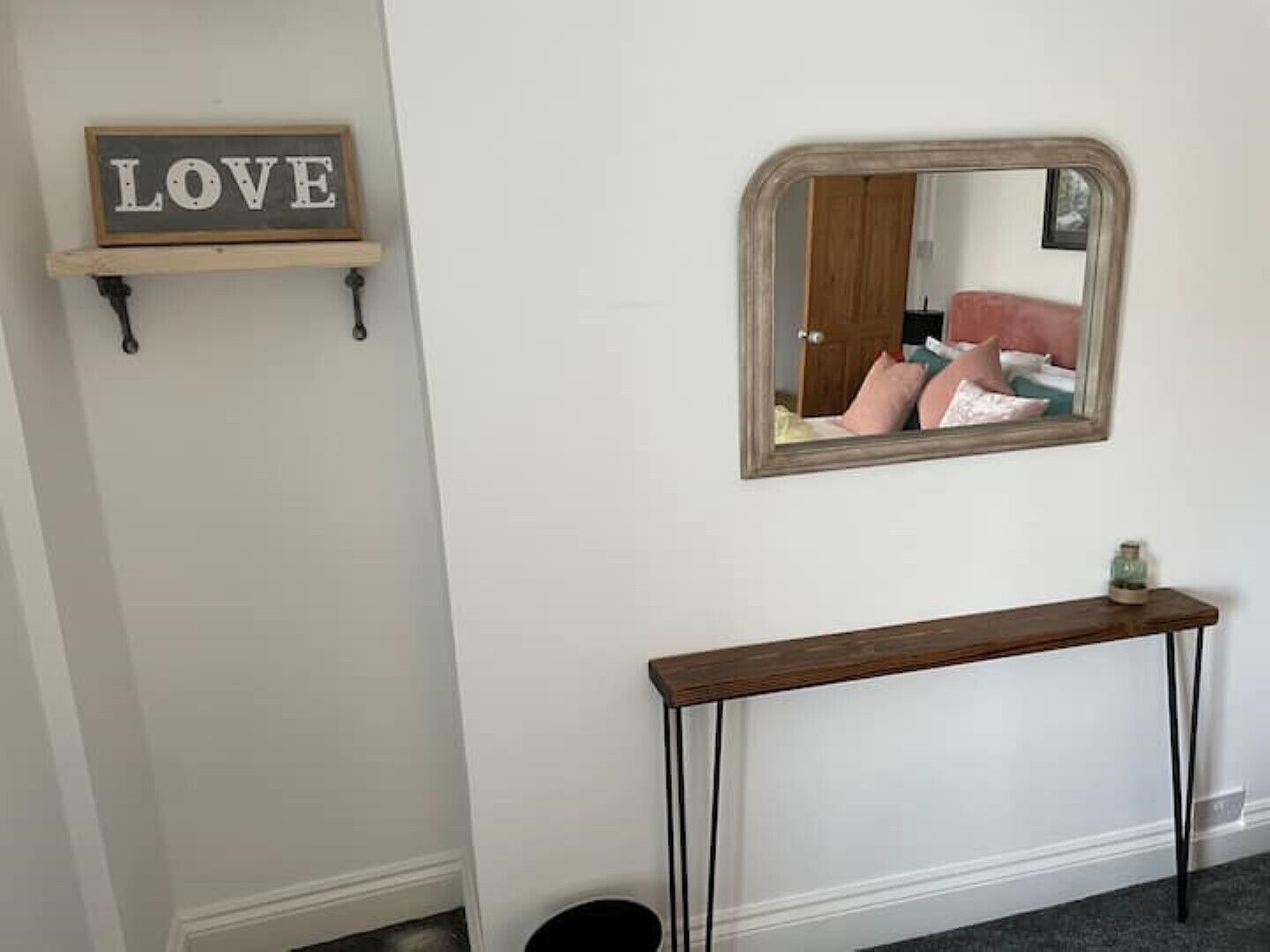 Un couloir avec une console en bois, un miroir et un panneau mural sur lequel est écrit le mot « AMOUR ».