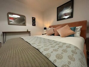 Un dormitorio ordenado con una cama grande, una mesita de noche, un espejo y un cuadro en la pared.