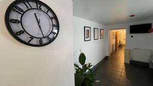 Un couloir avec une grande horloge murale, des tableaux encadrés et une plante en pot.