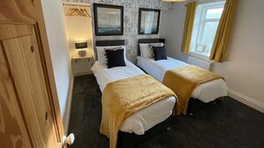 Une chambre d’hôtel avec deux lits, une armoire en bois, une fenêtre avec des rideaux et une lampe suspendue.
