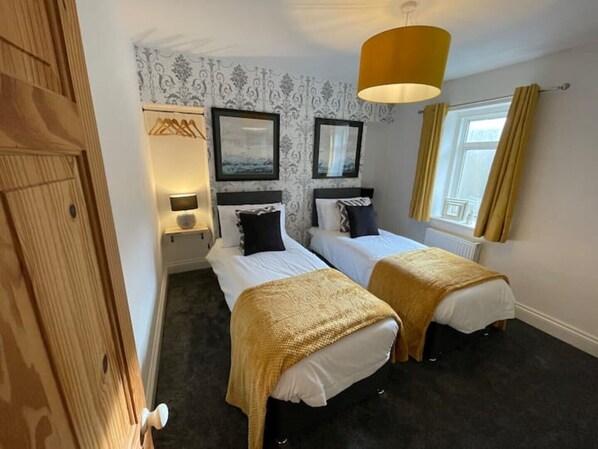 A hotel room with two beds, a wooden wardrobe, a window with curtains, and a hanging lamp.