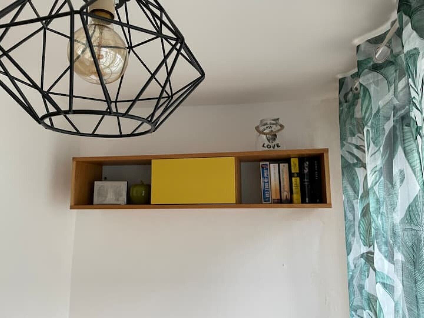 A room with a geometric metal light fixture, a wooden shelf with books and decorative items, and a wall with a 'Love' sign.
